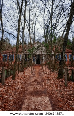 The facade of an abandoned kindergarten in the Chernobyl radioactive zone. Autumn foliage on the ground. Trees in front of an old house.
