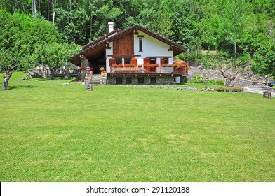 Facade Of The Alpine Chalet With A Grass Field On Summer