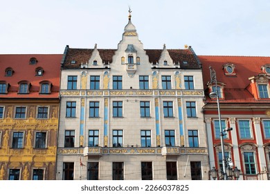 Facade of an ancient architectural buildings with white, red and yellow walls, tall windows, decorative elements and red roofs. Historical architecture. Old town. Poland, Wroclaw, January 2023.