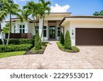 Facade of a beautiful house, with a front garden made up of palms, short grass and tropical plants, in Coral Ridge in Miami, driveway, sidewalk and street