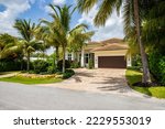 Facade of a beautiful house, with a front garden made up of palms, short grass and tropical plants, in Coral Ridge in Miami, driveway, sidewalk and street