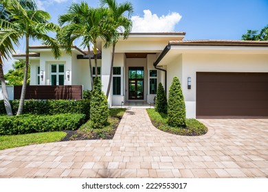 Facade of a beautiful house, with a front garden made up of palms, short grass and tropical plants, in Coral Ridge in Miami, driveway, sidewalk and street