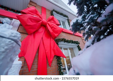 Facade Of A Brick Cottage In New Year's Decorations. Big Red Bow On The Wall Of The House. Christmas Tree Along The Window.