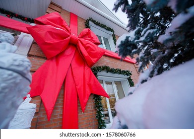 Facade Of A Brick Cottage In New Year's Decorations. Big Red Bow On The Wall Of The House. Christmas Tree Along The Window.