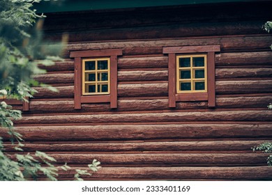 The facade of the building is made of rounded logs with brown dark window frames. Architectural structure and design. Windows in the house. High quality photo