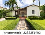 Facade of a colonial-style house with a beautiful front garden, with a path to the main door, driveway, tiled roof, located in the Granada neighborhood in the city of Coral Gables, palm trees and priv