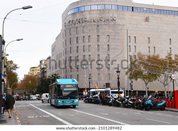 Facade of an El Corte Ingles Shopping Center.\
Scania hybrid bus for Airbus service by Monbus incorporates for\
Airport Barcelona. Official Shuttle Bus Airport Barcelona. Dec 19,\
2021, Spain, Barcelona.