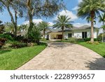 Facade of elegant house with park with short grass, tropical plants, palms, trees, sidewalk, driveway, blue sky in the background, in the pinecrest neighborhood