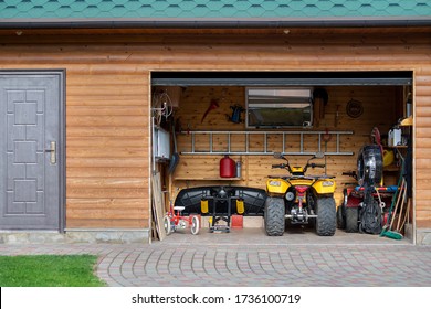 Facade Front View Open Door ATV Quad Bike Motorcycle Parking Messy Garage Building With Wooden Siding At Home Driveway Backyard And Lawn Path. House Warehouse For Tools And Equipment . Garage Sale