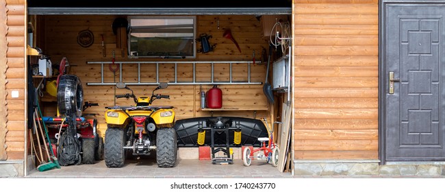 Facade front view open door ATV quad bike motorcycle parking messy garage building with wooden siding at home driveway backyard and lawn path. House warehouse for tools and equipment . Wide panoramic - Powered by Shutterstock