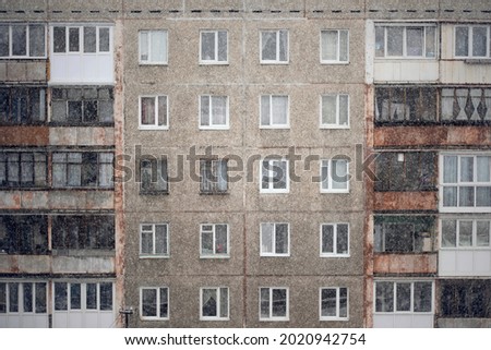 Facade of a grey multi-storey soviet panel building in the fallen snow. Russian old urban residential houses with windows. Typical russian neighborhood.