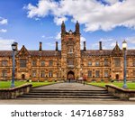 Facade of historic classic building of traditional brick and mortal university in Australia - main facade with steps and alley leading to the main tower and entrance gate under blue sky.