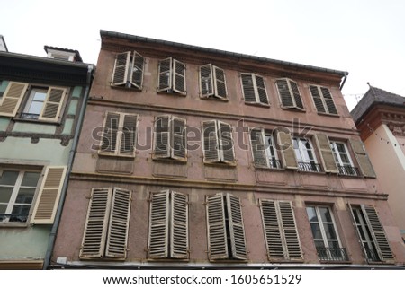 Facade of a historical residential house in Colmar, Alsace, France. The windows have shutters, some of them are closed. The facade itself is stained by water and time.