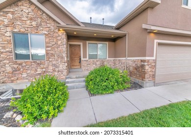 Facade of a house with shrubs, brown stone veneer siding, and garage - Shutterstock ID 2073315401