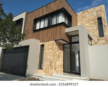 Facade of a modern house with avant-garde architecture, with stone, wood and metal on its facade in the background of blue sky and in its surroundings vegetation and plant - Shutterstock ID 2316899157