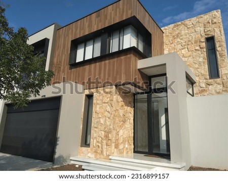 Facade of a modern house with avant-garde architecture, with stone, wood and metal on its facade in the background of blue sky and in its surroundings vegetation and plant