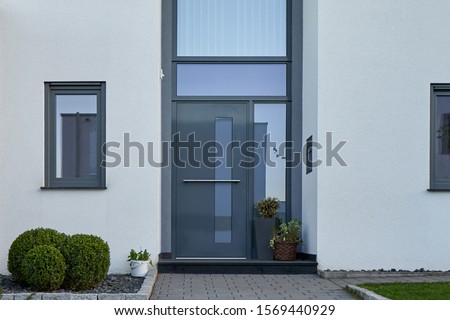Facade of a modern house with a gray front door and potted flowers.