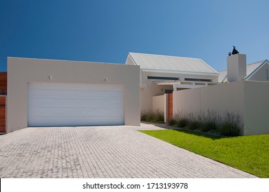 Facade of a modern house from the street with white walls, lavender plants, green lawn and garage driveway