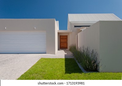 Facade of a modern house from the street with white walls, lavender plants, green lawn and garage driveway