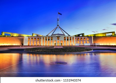 Facade of new parliament house in Canberra on capitol hill at sunset with bright illumination reflecting in blurred waters of pool. Public building free for admission by australians and guests.