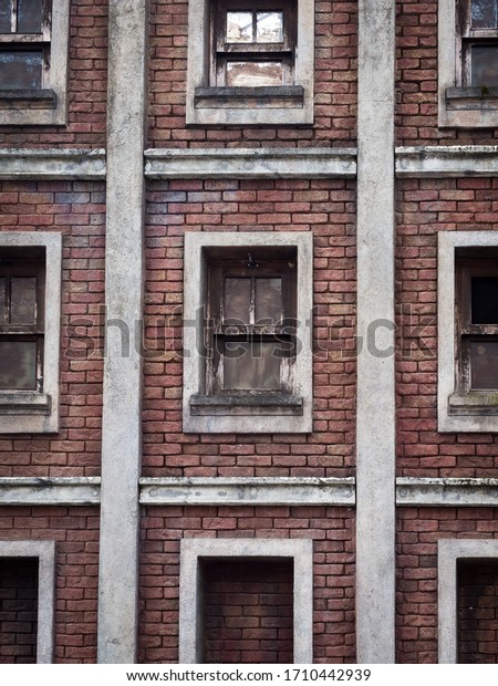 Facade of old abandoned brick house. Windows\
divided by white\
squares.