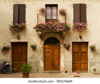 Facade of old house in Pienza with windows,  balcony with flowers,  wooden doors, plants. Tuscany, Italy