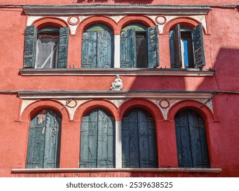 Facade of an old palace painted red, with arched windows, green shutters and a small bas-relief depicting a Pietà, Piscina San Samuele, San Marco sestiere, Venice, Veneto, Italy - Powered by Shutterstock