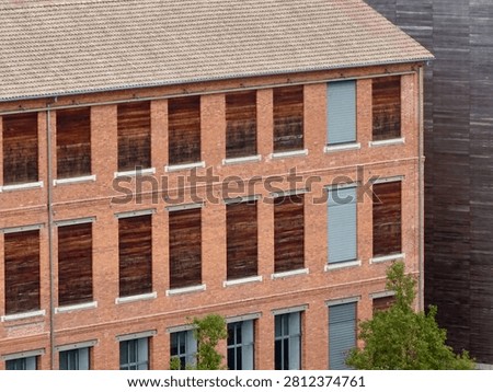 Facade of an old red brick textile factory in Mulhouse with rows of windows boarded up with wood, industrial heritage in Alsace, France