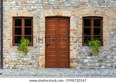 Facade of old renovated house with stone wall. A wooden door and two closed windows.