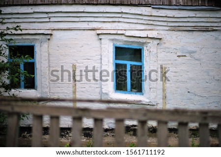 Facade of an old rural house with blue window frames. Ancient architecture in greek national colors. Old deformation of the wall structure caused by subsidence.