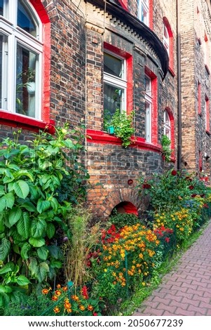 Facade of an old, traditional, silesian brick block house in Nikiszowiec, Katowice, Poland. Small, colorful garden in front of the building. 