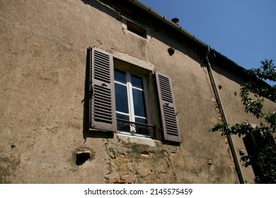 The facade of an old, uninhabited and abandoned house in Burgundy (France). A window with brown wooden shutters. The wall is damaged, decrepit. The sky is blue.
