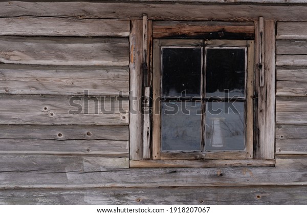 The facade of an old wooden log building with a\
small window divided into 4 parts and inside you can see a cup\
placed on a table