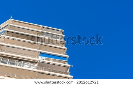 the facade of a residential building with multiple terraces and blue awnings under a clear sky.