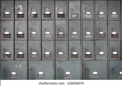 Facade of rows of old grungy green colored metal locker boxes on a wall.