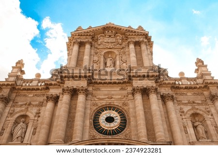 Facade of Saint-Paul-Saint-Louis church in Paris, showcasing baroque architecture, ornate sculptures, a central clock, and a backdrop of blue sky.