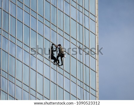 Facade of a skyscraper with steeplejack. Window washer working high up on modern office building