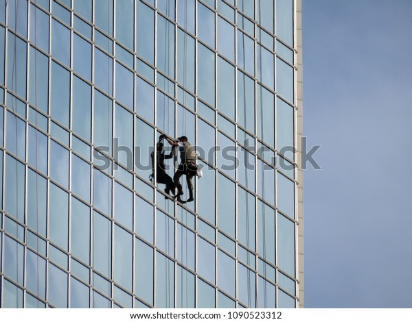 Facade of a skyscraper with\
steeplejack. Window washer working high up on modern office\
building