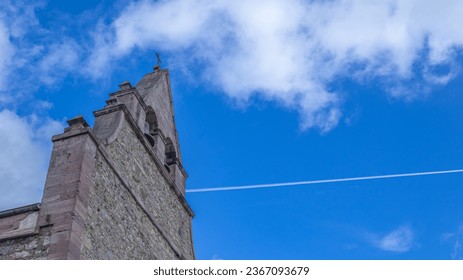 Facade and tower of a church, in the background blue sky with a contrail produced by an airplane. - Shutterstock ID 2367093679