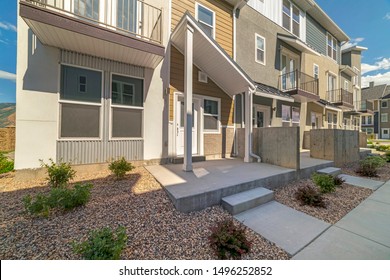 Facade of townhomes with balconies and rocky yards viewed on a sunny day