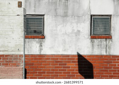 A facade with two plain windows on a weathered white concrete wall with a red brick base, a perfect example of the effects the weather have on the built environment. Good for post about urban decay
