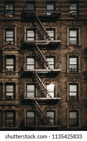 Facade of a typical New York block of flats with fire escape at the front, sun reflects in the windows.

