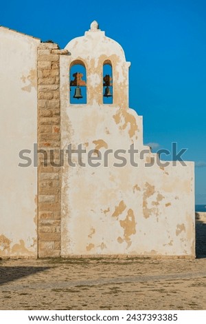 Facade of a very old historica crumbling wall with an arched top two windows containing large bronze or brass bells church in Sagres Portugal Algarve region