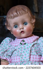 Face of antique doll with blue eyes and rosy cheeks, wearing a white dress with pink flowers.
