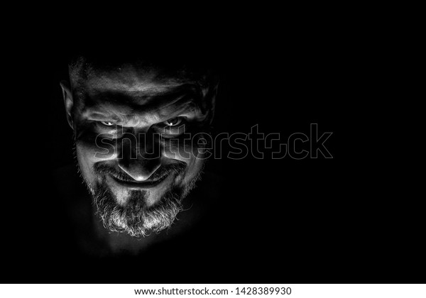  Face with a bearded man\
grimace against a dark background with sharp shadows. Comedic,\
fabulous villain or negative character conception with copy\
space.