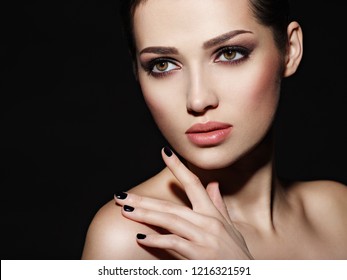 Face of a beautiful girl with fashion makeup and black nails posing at studio over dark background