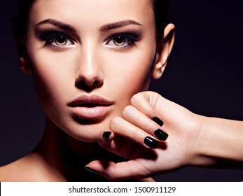 Face of a beautiful girl with fashion makeup and black nails posing at studio over dark background