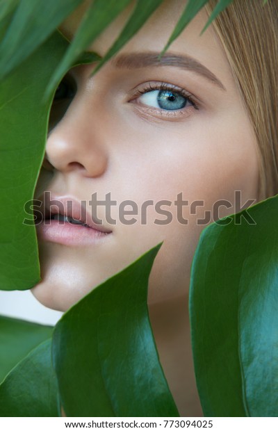 Face of\
beautiful young woman with clean perfect skin covered by leaves.\
Portrait of beauty model with natural nude make up and long\
eyelashes. Spa, skincare and wellness. Close\
up.