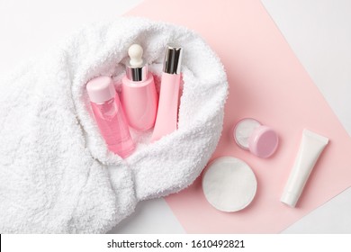 Face care products (tonic or lotion, serum, cream, micellar water, cotton pads) covered in towel on pink, powder background. Freshness and face care. Skin cleansing and anti-age care. Female cosmetics