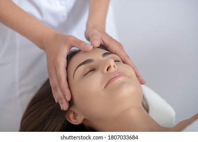 Face care. Professional massage therapist massaging forehead of customer